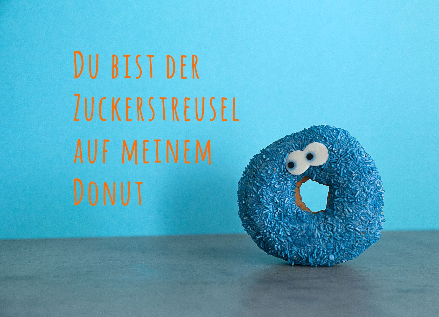 Ein Donut mit blauen Zuckerstreuseln und Augen steht vor einem blauen Hintergrund. Auf der Karte steht der Spruch: Du bist der Zuckerstreusel auf meinem Donut.