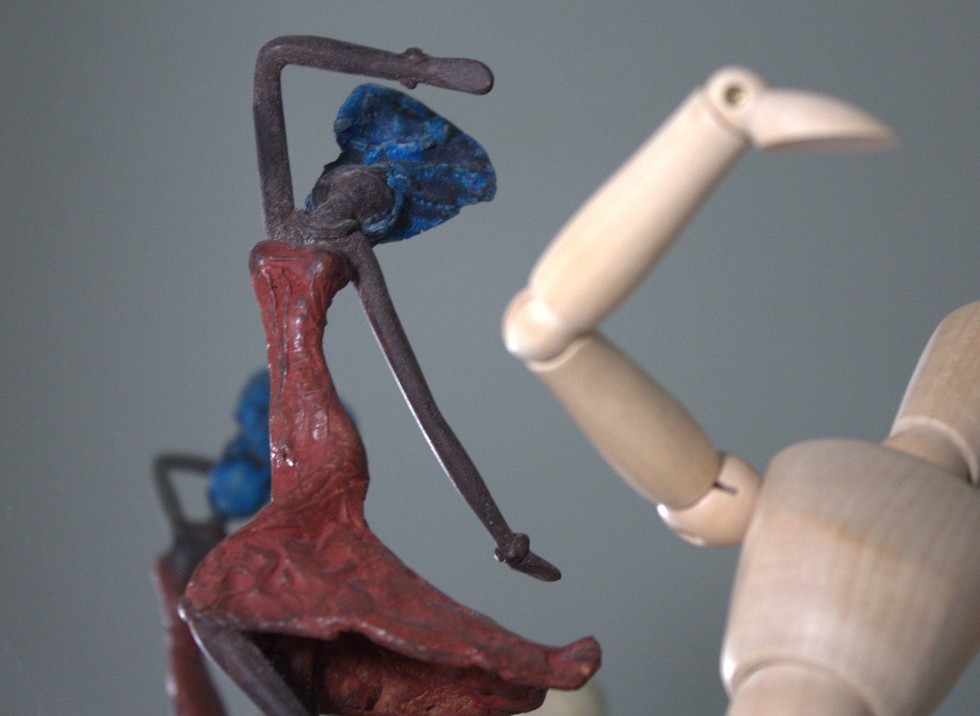 Two models of figures dancing, one a Black woman in a red dress and blue hat, second a wooden figure