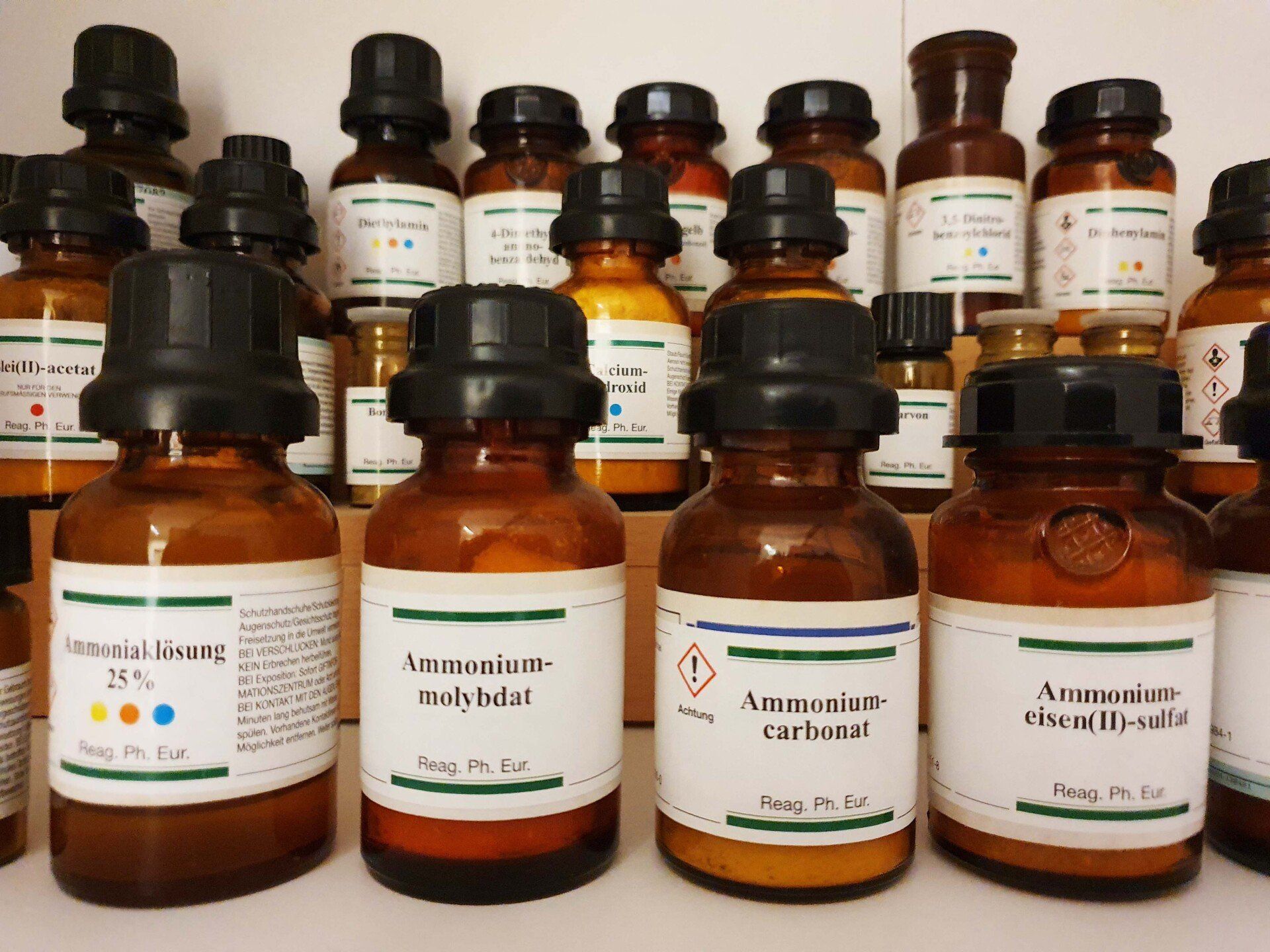 Apothekenregal mit braunen Chemie- und Arzneiflaschen, beschriftet mit Inhaltsstoffen.