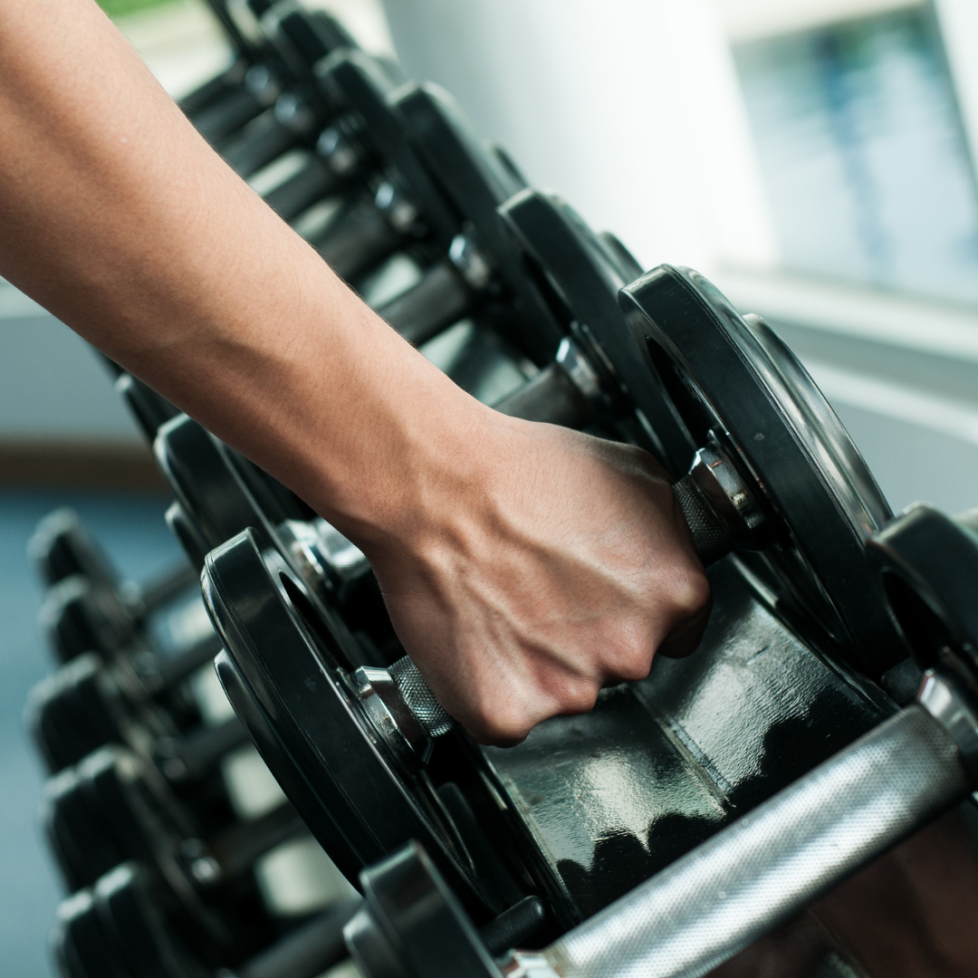rechte Männerhand die nach einer Hantel auf der Aufbewahrung greift