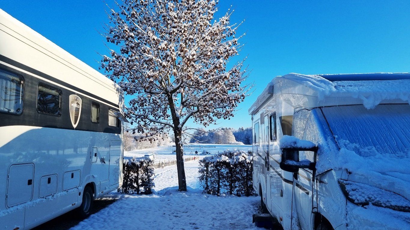 Baum zwischen zwei Wohnmobilen im Schnee bei Sonnenschein