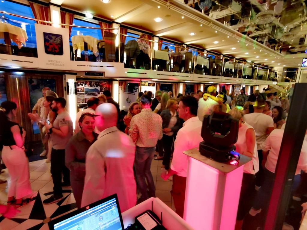 Ausgelassene Partystimmung und eine volle Tanzfläche im illuminierten Innenraum des Schiffes mit DJ Tom.