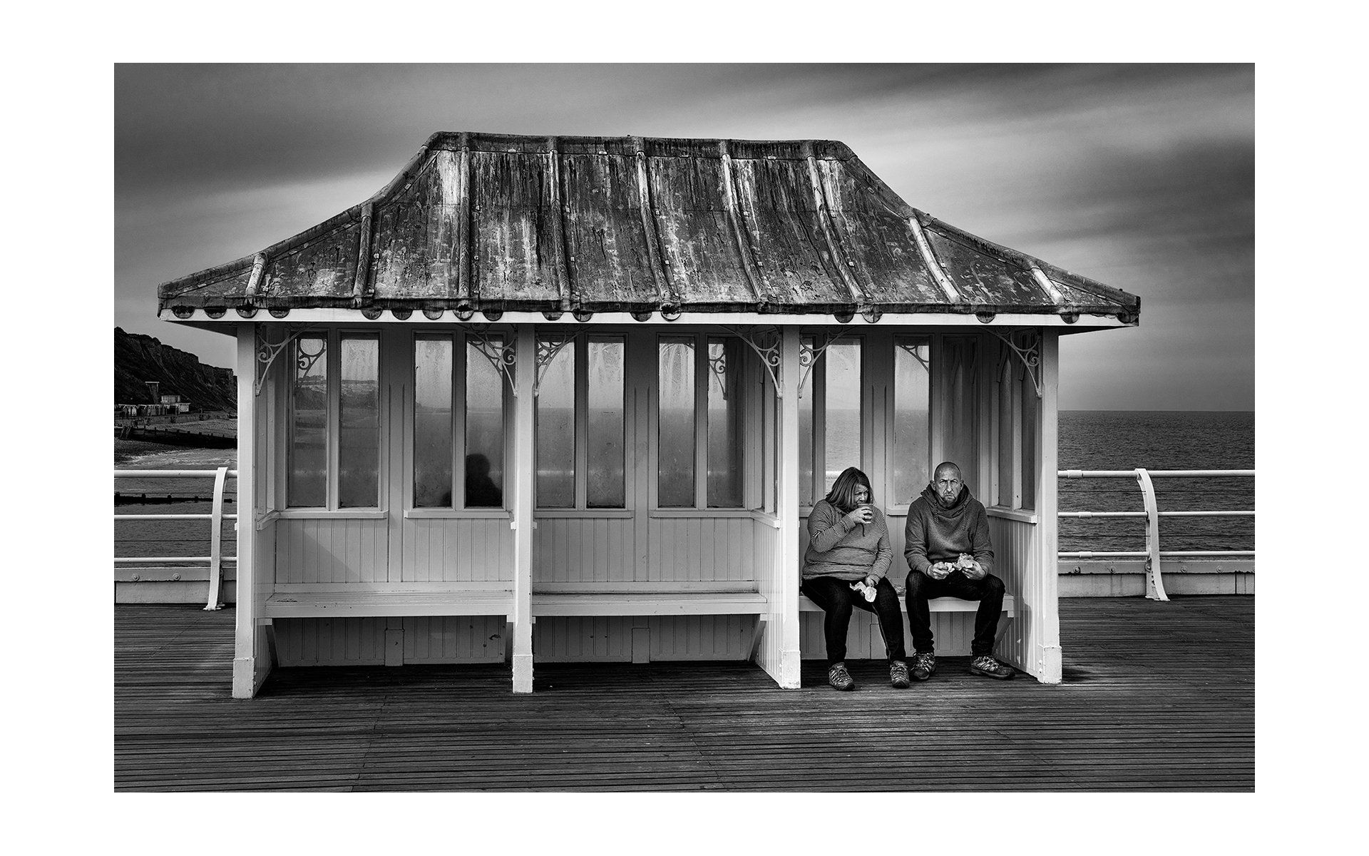 a couple sitting in a beachside shelter out of the wind, and rain