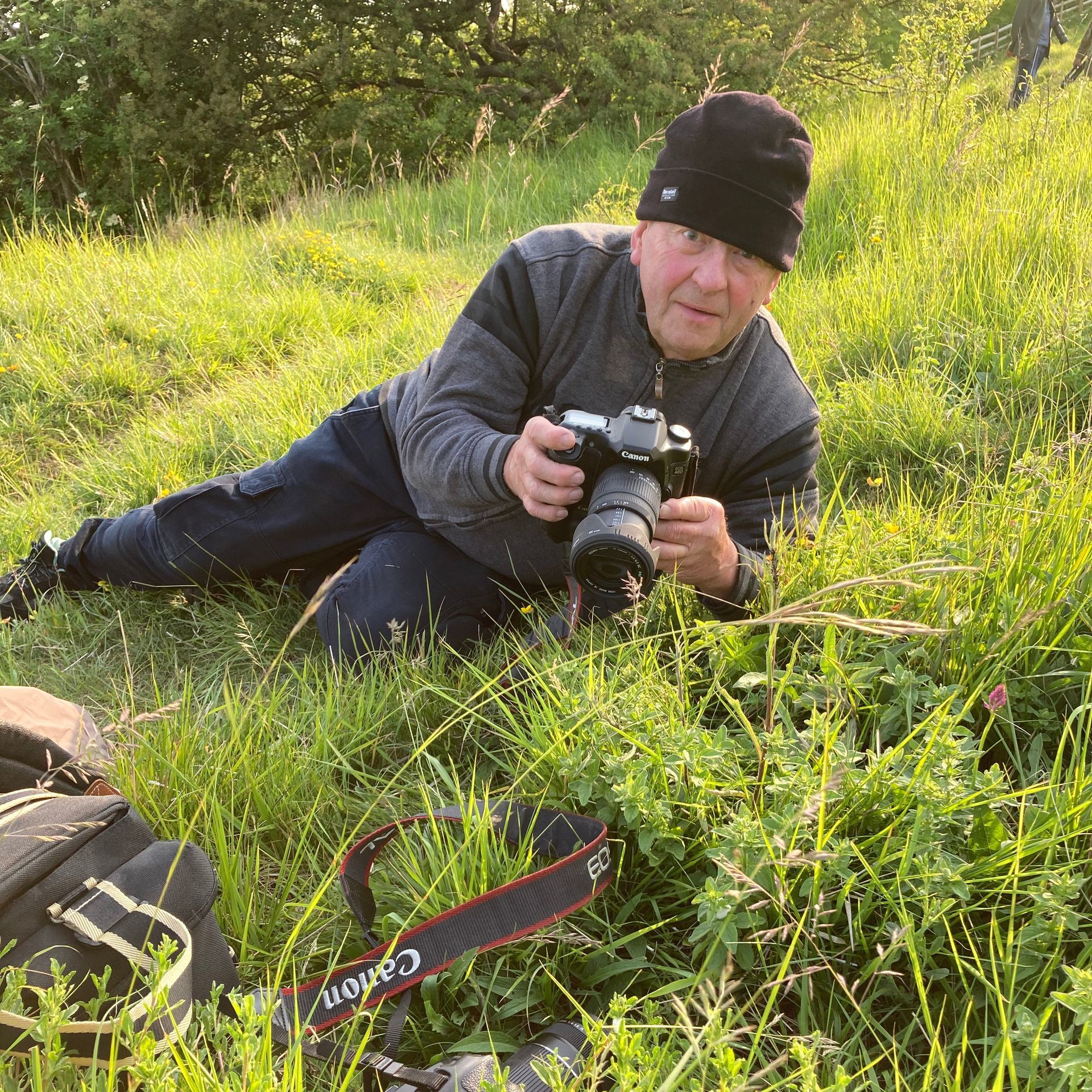 A photographer laying in the grass taking a macro shot.