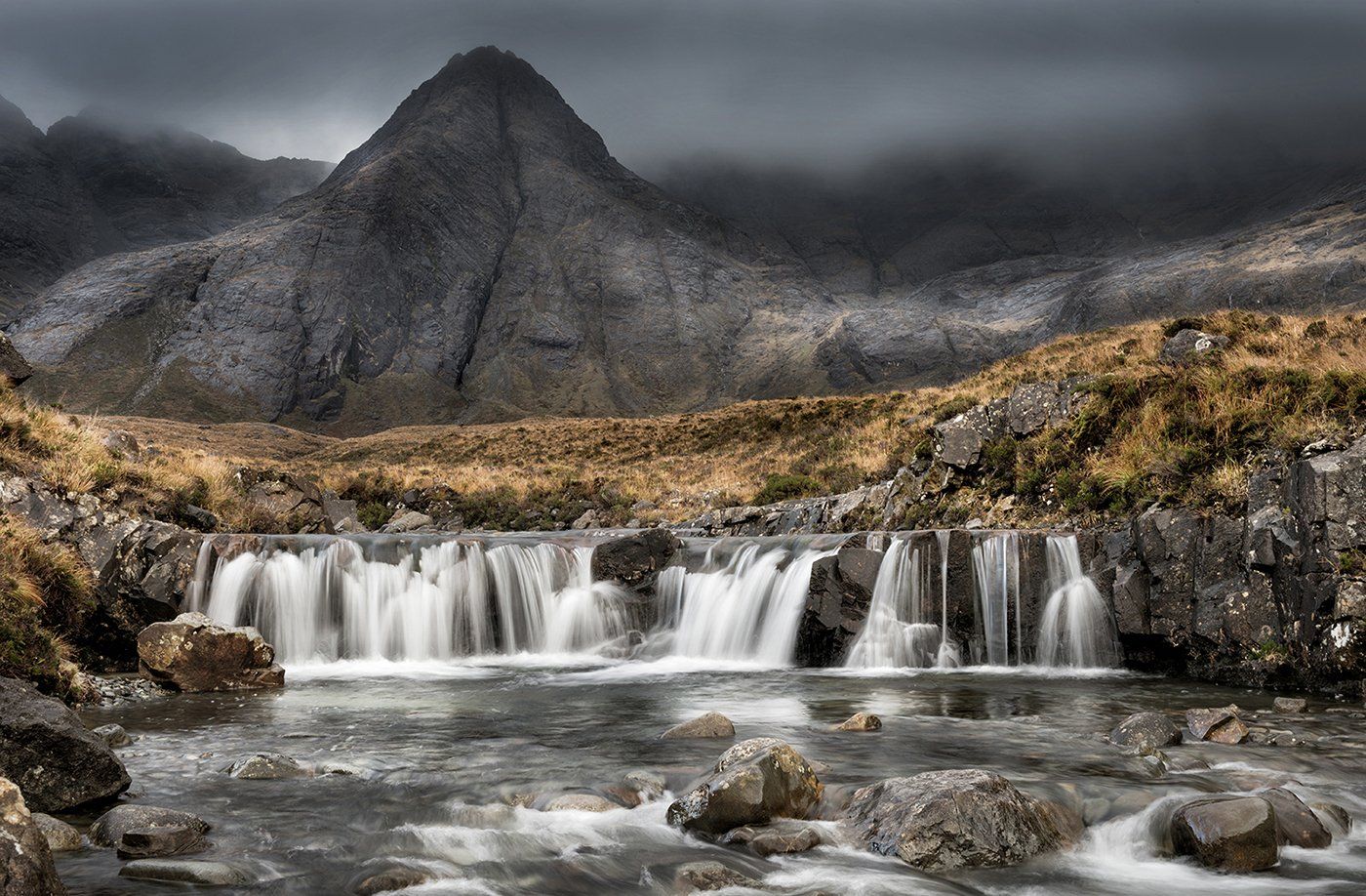 a view of a body of water on the isle of skye beneath a mountain