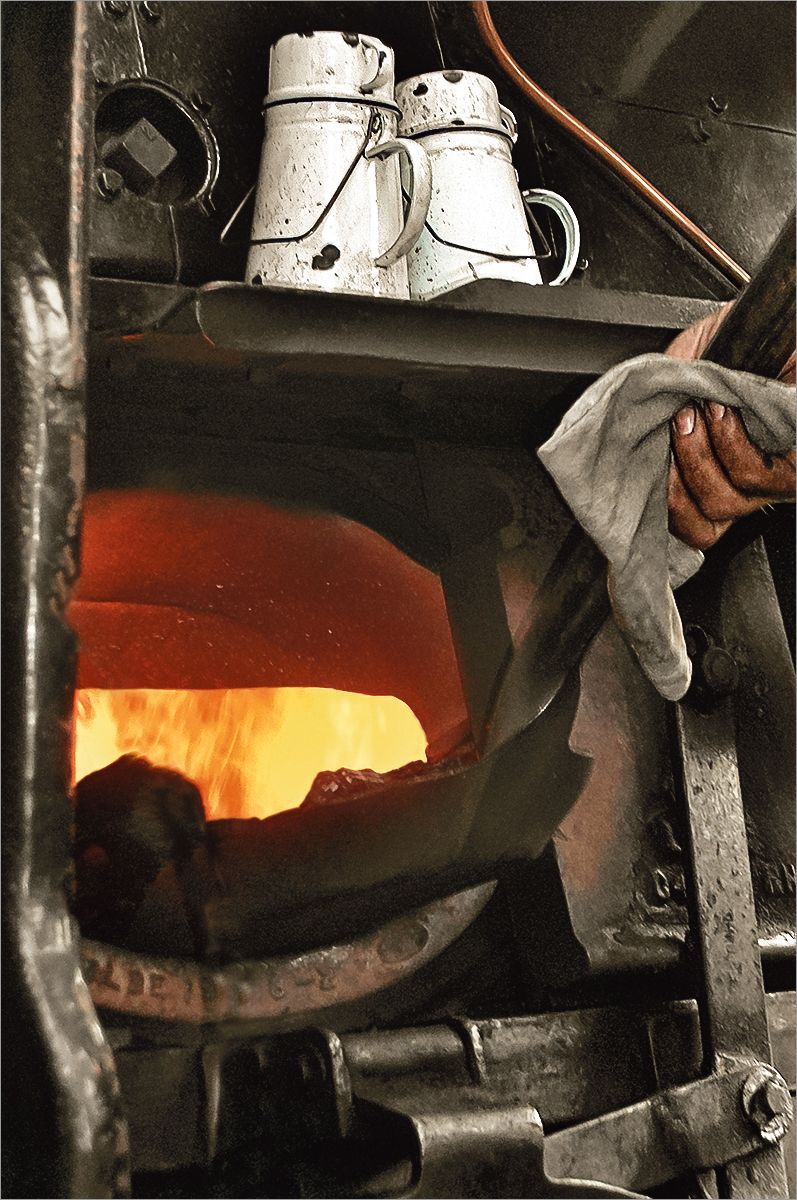 a shovel of coal being fed into a steam locomotive fire