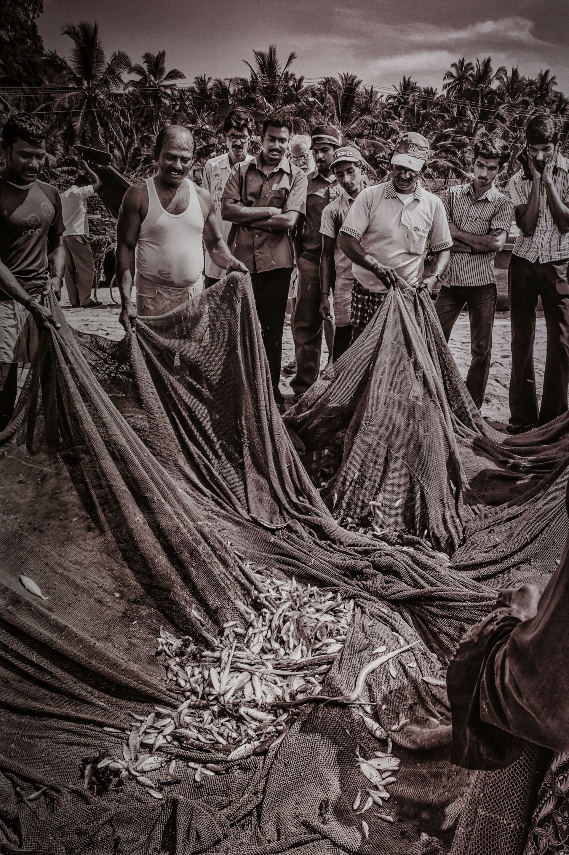 a group of fishermen gazing at a meagre catch in a net