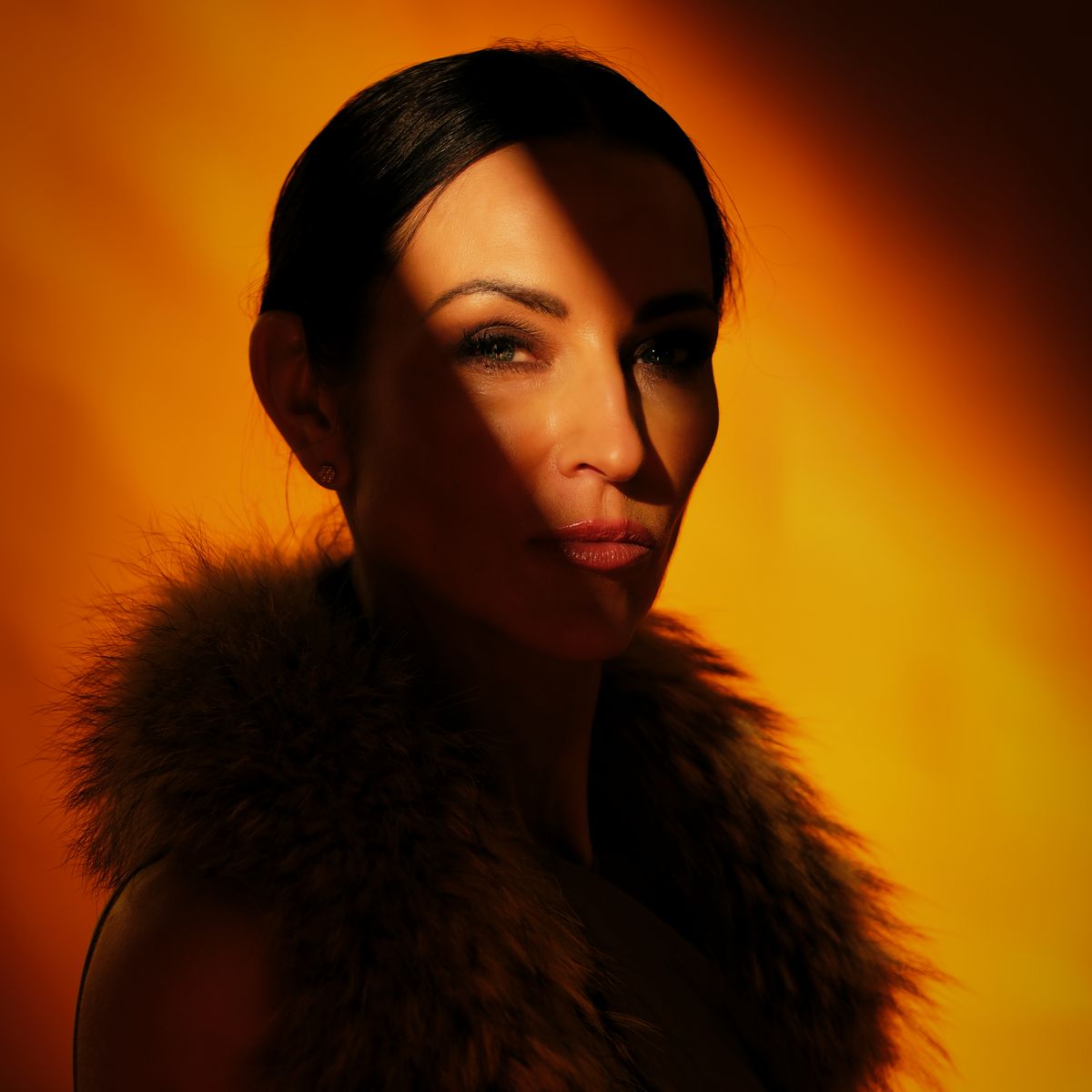 A female model lit by a diagonal ray of light on an orange background