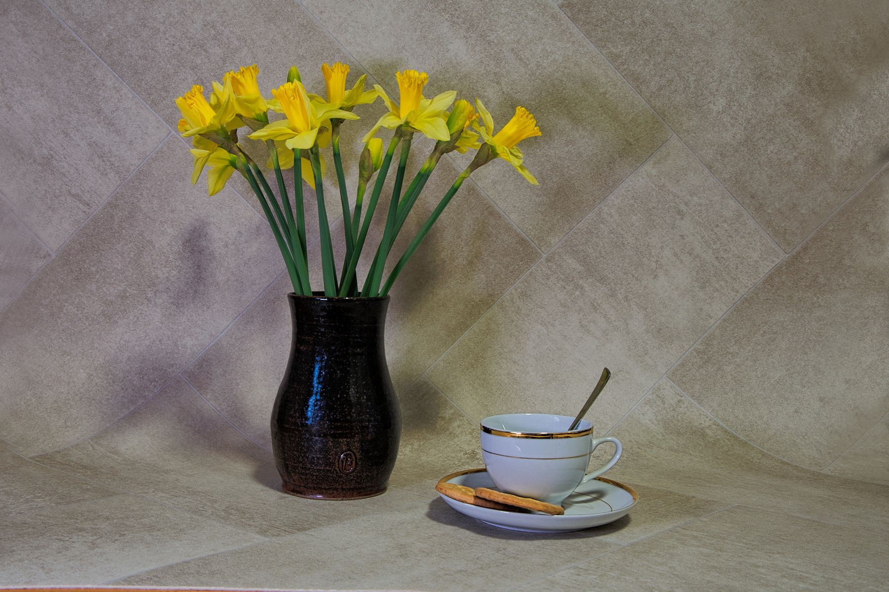 A still life image of a vase of daffodils, with a cup and saucer