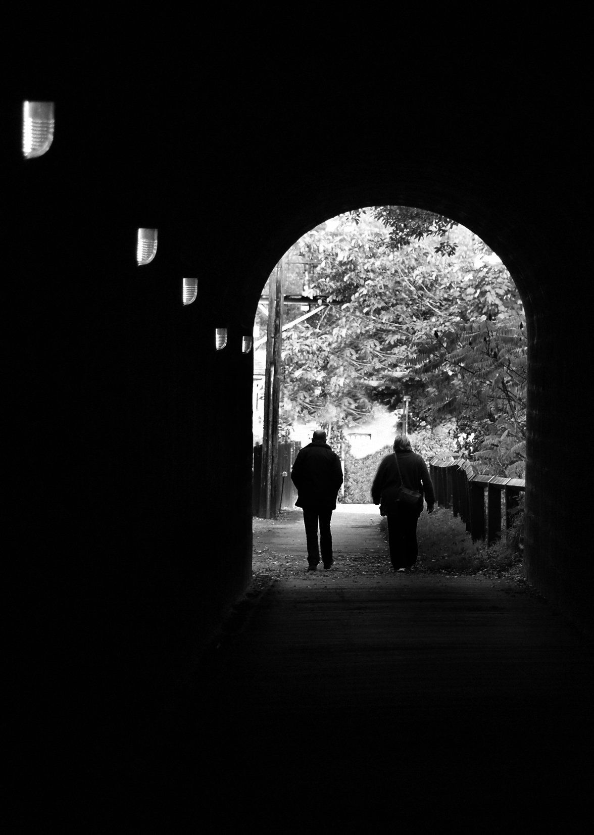 a dark tunnel with a couple walking toward the entrance tranentrance