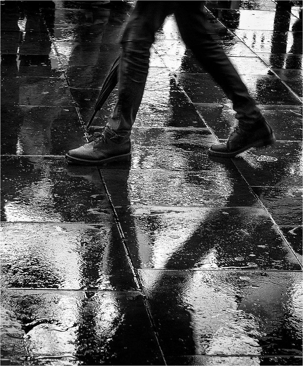 A man's legs, and feet shadowed on a wet pavement