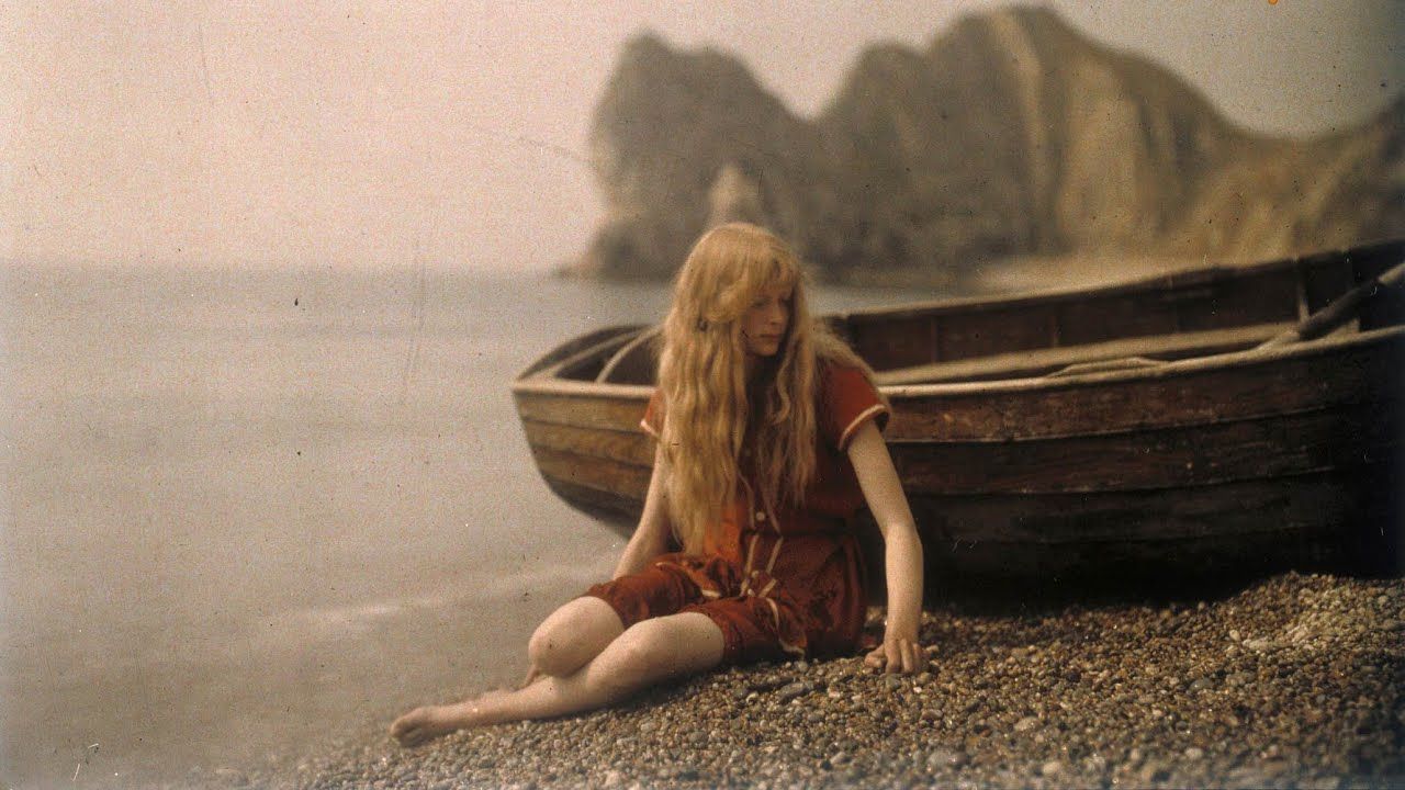 a girl on a pebble beach beside a boat