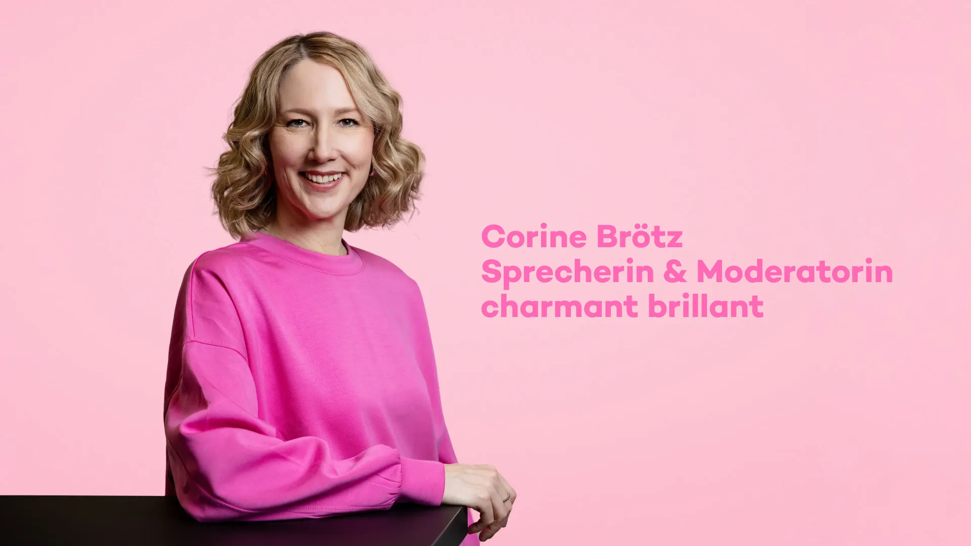Sprecherin Corine Brötz in einem pinken Oberteil vor einem rosa Hintergrund. Text:
Corine Brötz
Sprecherin & Moderatorin
charmant brillant