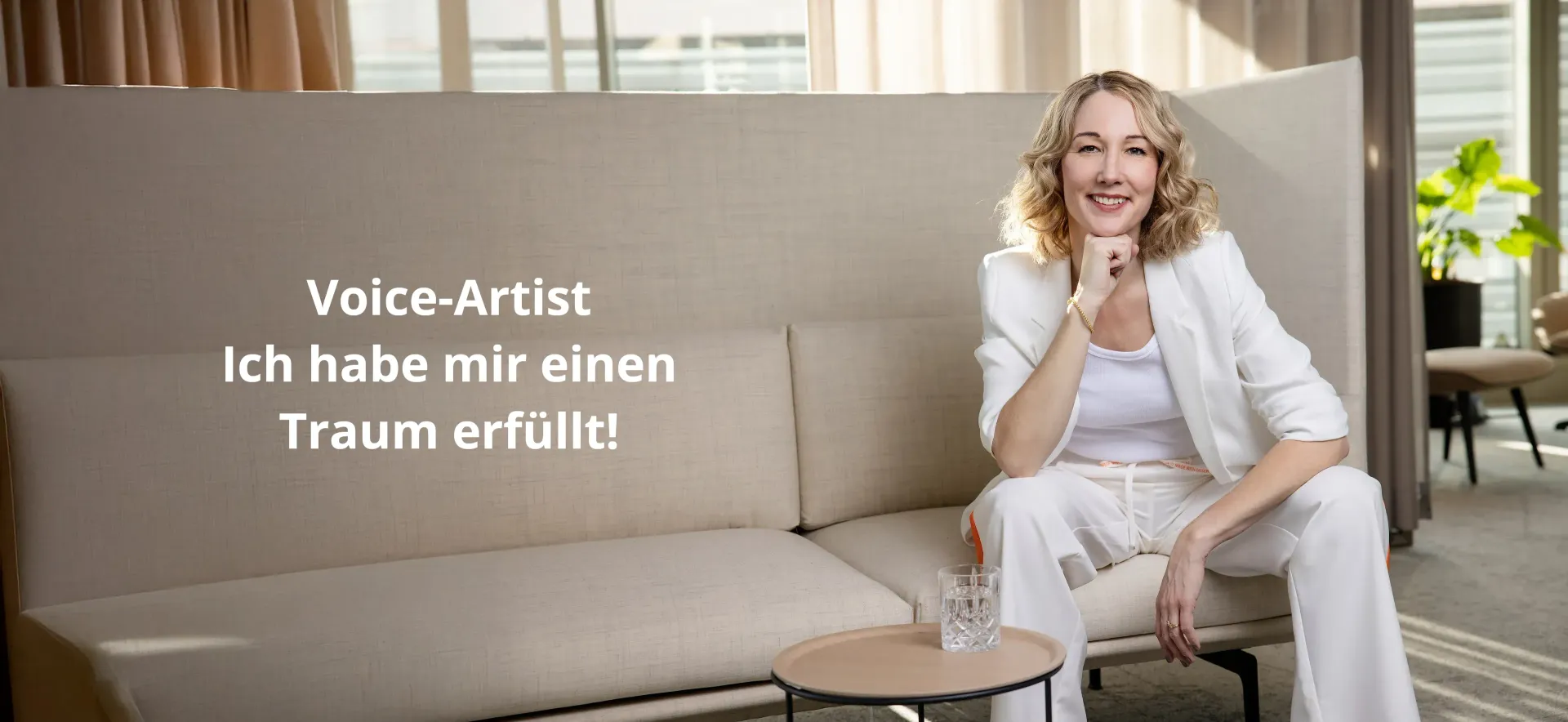 Corine Brötz. Voice-Artist
Corine sitzt in einem weißen Hosenanzug auf einem beigen Sofa.