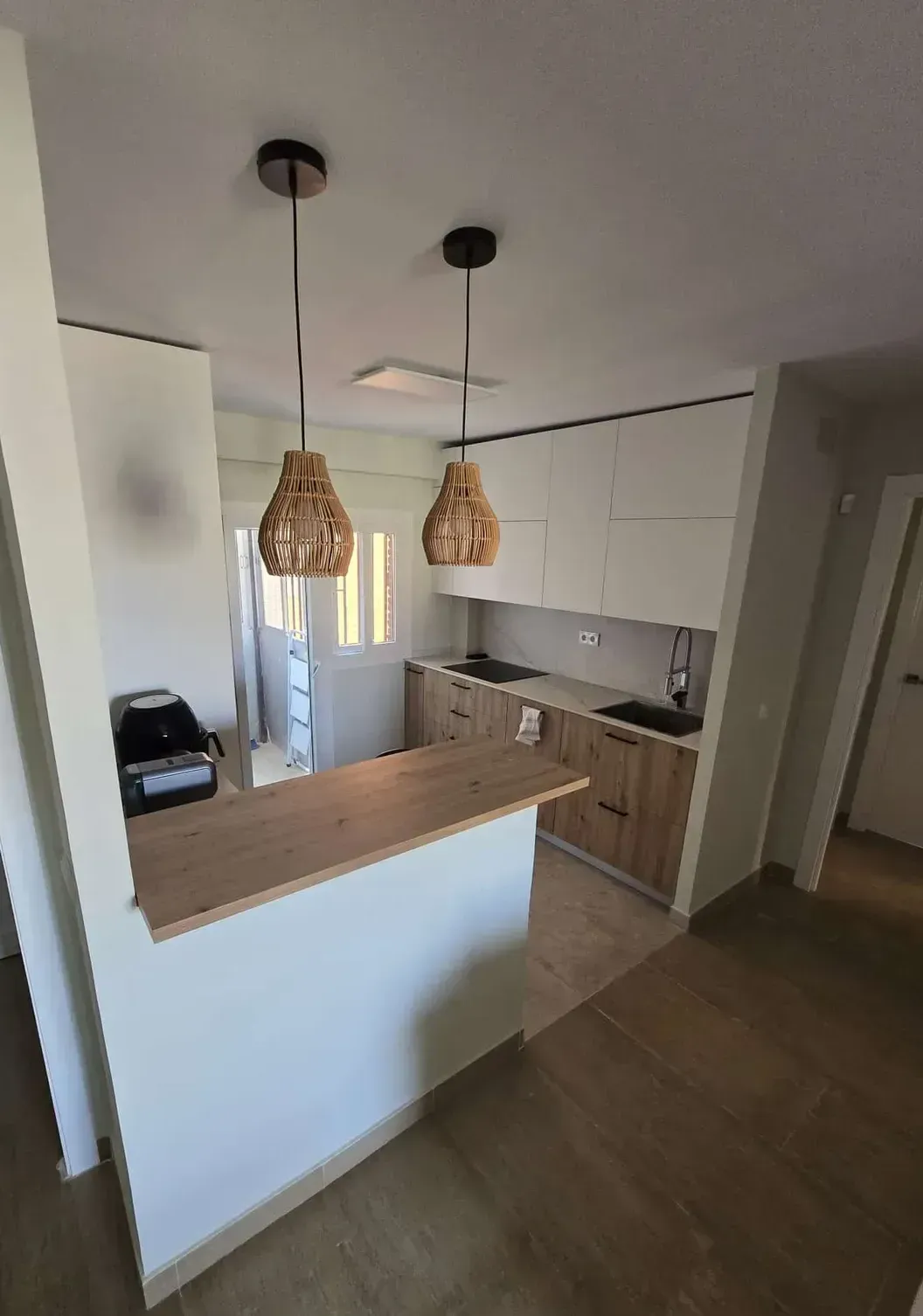 Cocina reformada con mobiliario en blanco y madera, barra americana y diseño moderno en vivienda de