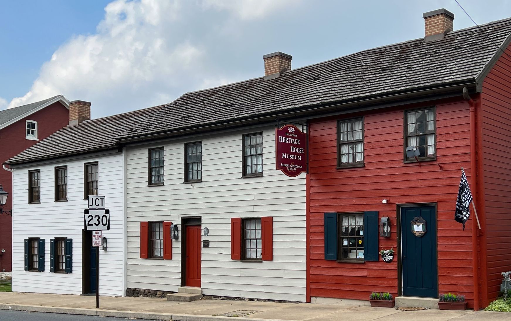 angled view of the front of Winters Heritage House with focus on 47 E High Street red building. The main entrance as of November 2023. A hanging sign reads Winters Heritage House Museum & Seibert Genealogy Library.