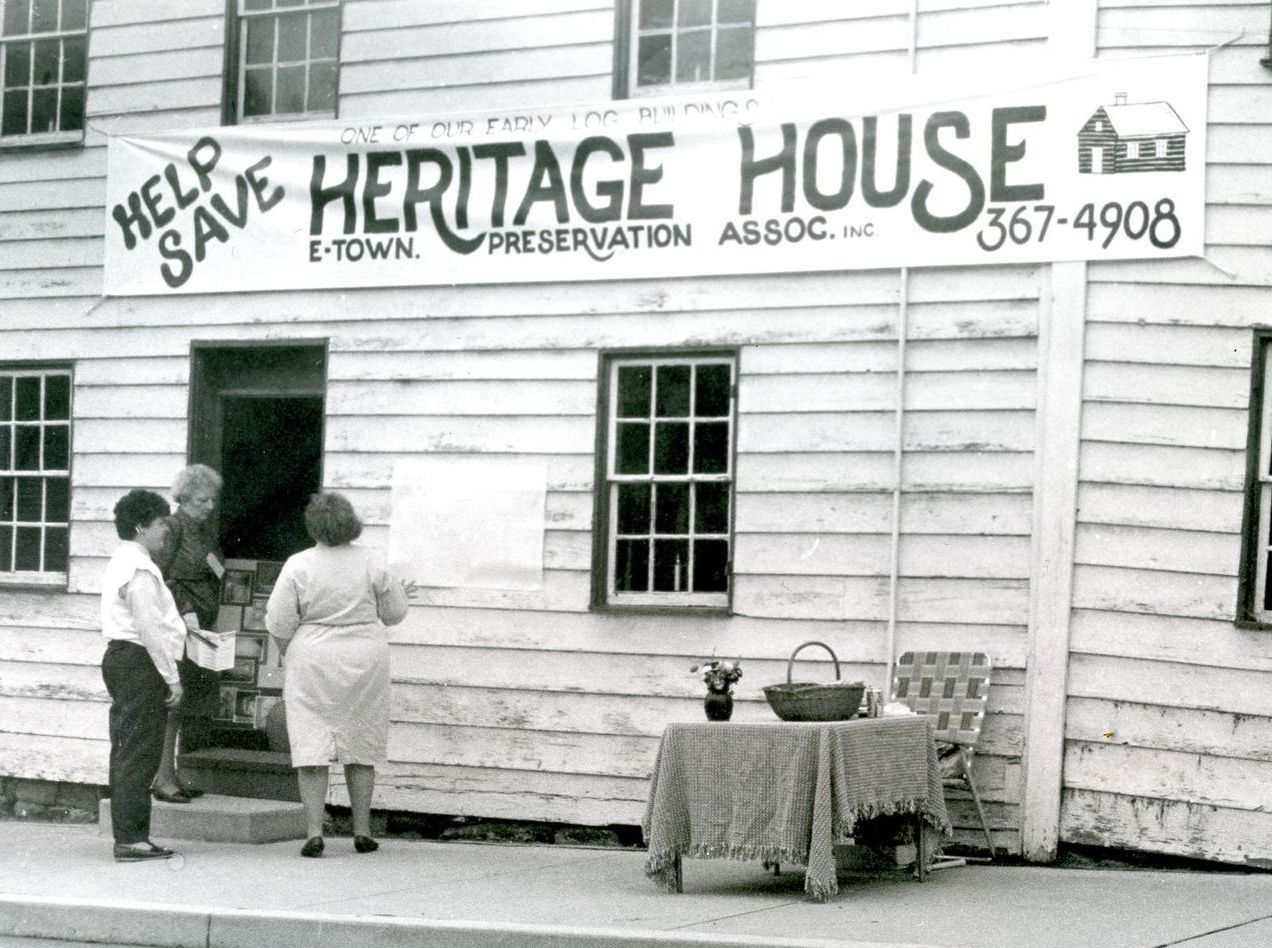 black and white photo of Heritage House in the late 1980's. House looks old and tattered. Three people gather talking by a sign-up sheet.