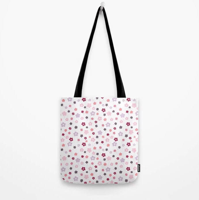 Tote Bag Tragetasche. Design und Produkt-Muster by Feinrosa. Die Tasche ist weiß mit zwei schwarzen Schulter-Trageriemen. Die Tote Bag mit Blumen-Muster ist mit zahlreichen kleinen, handgemalten und bunten Blümchen verziert. Die Blumen sind rot, apricot, zart lila, rosa und orange. Die Tote Bag ist bei Society6 erhältlich.