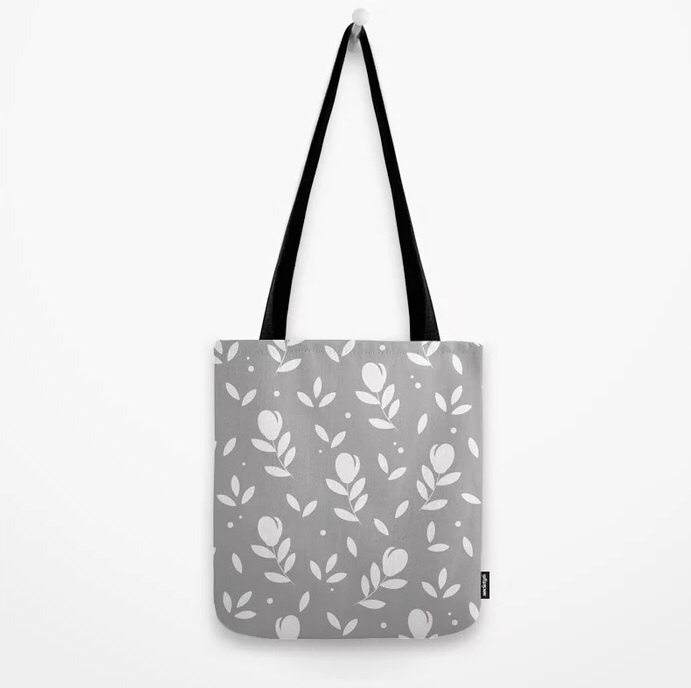 Tote Bag Tragetasche. Design und Produkt-Muster by Feinrosa. Die Tasche ist hellgrau mit weißem Blumenmuster und verfügt über zwei Schulter-Trageriemen. Die Tote Bag ist mit einem weißen Blumen-Muster verziert. Das Produktmuster stellt Tulpen mit zwei Blättern dar. Die modische Tote Bag ist bei Society6 erhältlich.