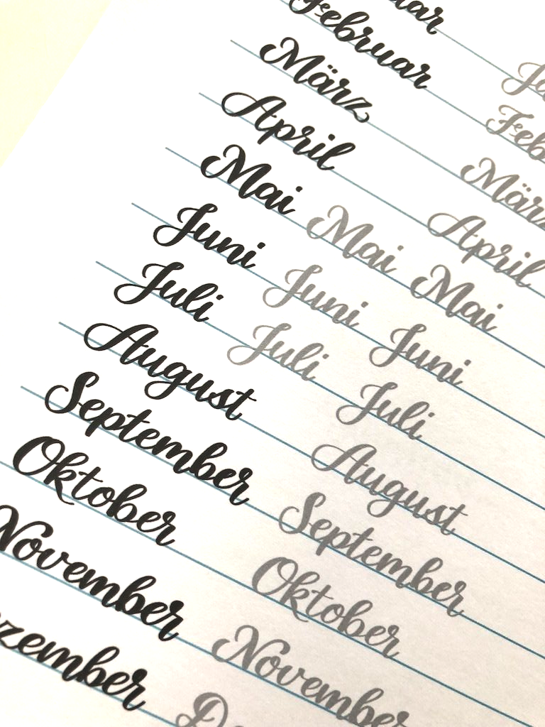 Vorlage zum Üben von Monatsnamen im Handlettering-Stil. Die 12 Monatsnamen sind schwarz mit einem Brushpen gelettert. Daneben wiederholen sich die Namen in hellgrauer Schrift.