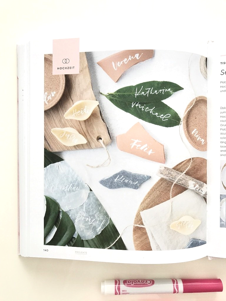Handlettering Hochzeits-Papeterie. Frau Hölle zeigt Ideen, wie unterscheidliche Materialien mit Handlettering beschriftet sind. Grüne Blätter, Pergament, Papier, Stein und Holz.