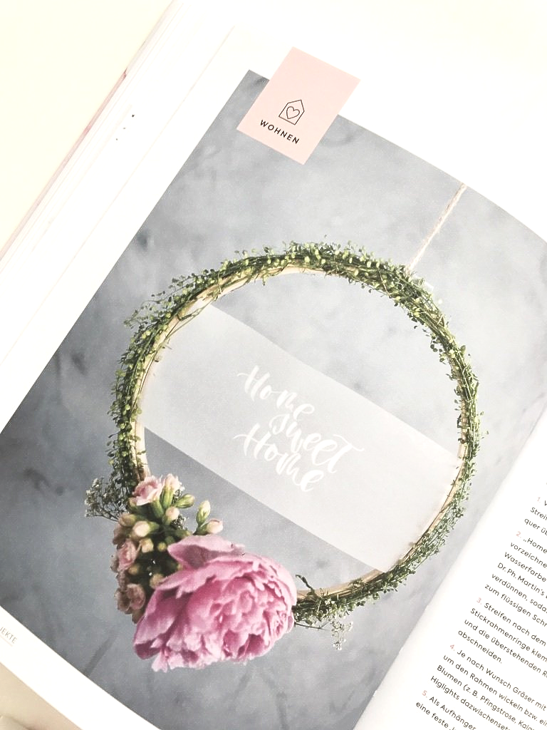 Blumenkranz mit rosafarbener Pfingstrose. Darin ist ein handgeschriebenes Lettering aufgehangen.