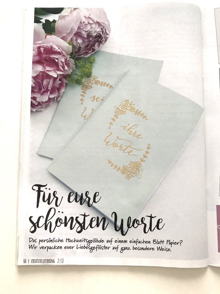 Pfingstrosen in rosa liegen auf einem Tisch. Daneben liegen zwei DIY Grußkarten, die mit einem goldfarbenen Marker im Handlettering-Stil beschriftet sind. Das Lettering ist mit goldenen Blumen und Blättern verziert.