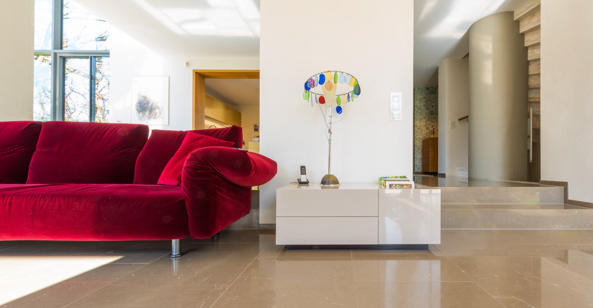 Ein Lowboard mit Fächern für Zeitschriften und mit Dekoobjekten, links daneben ein rotes Sofa, edles Wohnzimmer