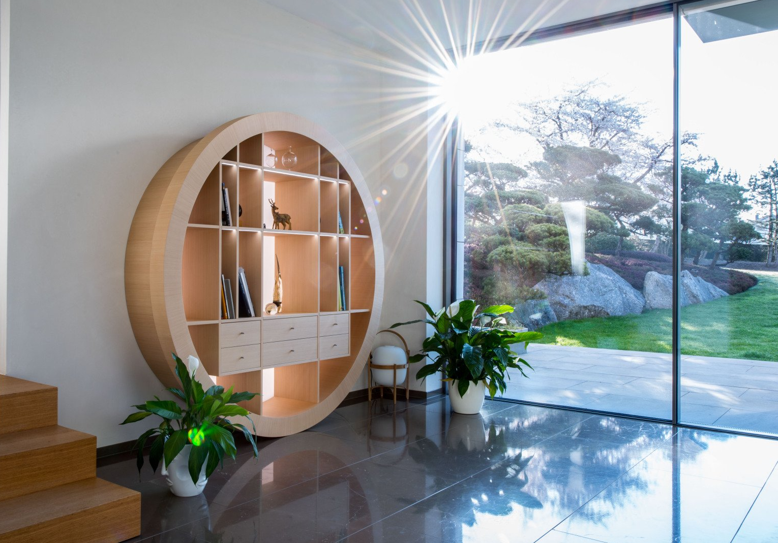Das runde Regal von BLEIER Lebensräume im Wohnzimmer, im Hintergrund ein gepflegter Garten