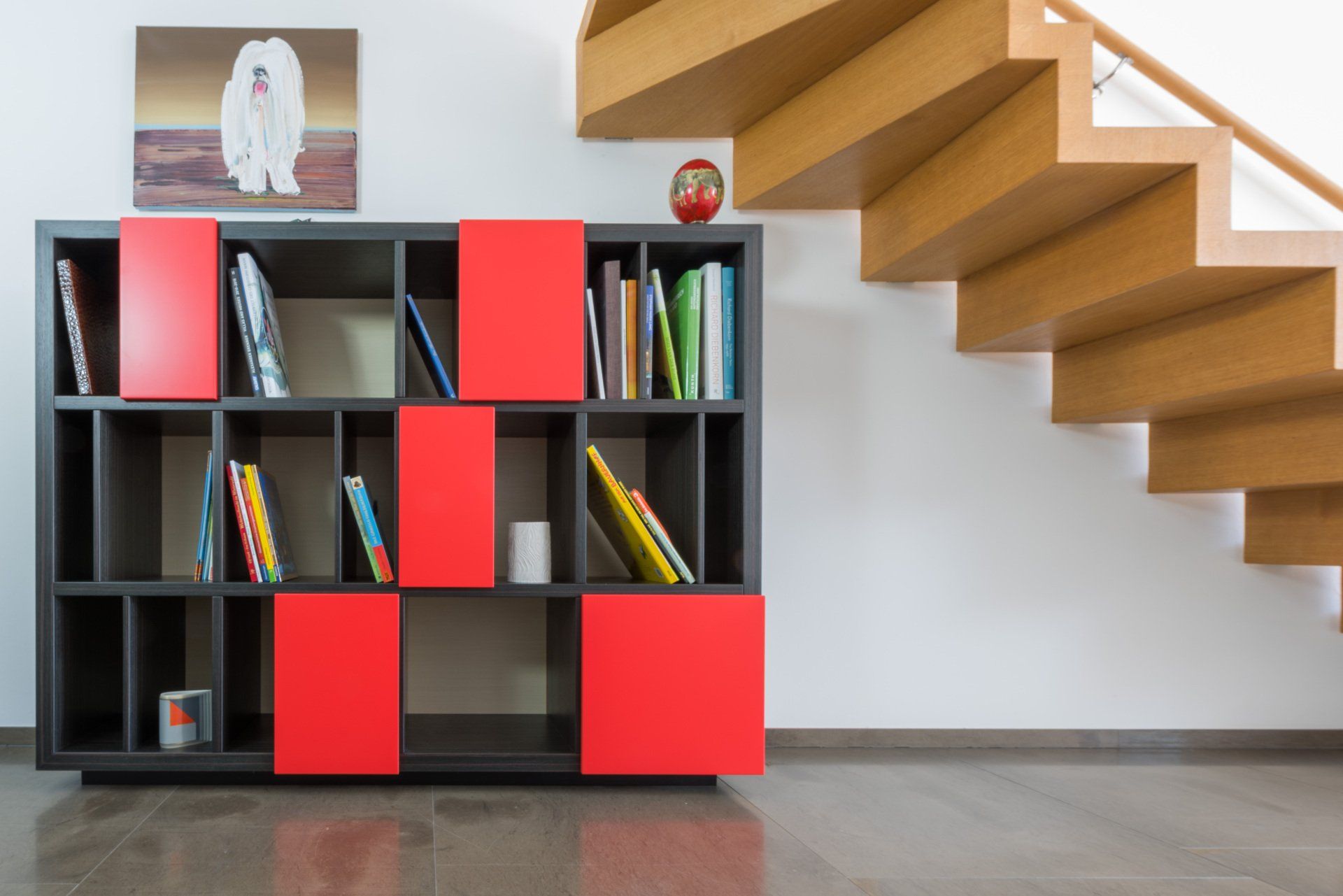 Regal aus Ebenholz von Schreinerei BLEIER Lebensräume, mit roten Fronten zum Verschieben auf edlem schwarzem Holz, rechts oben eine Treppe