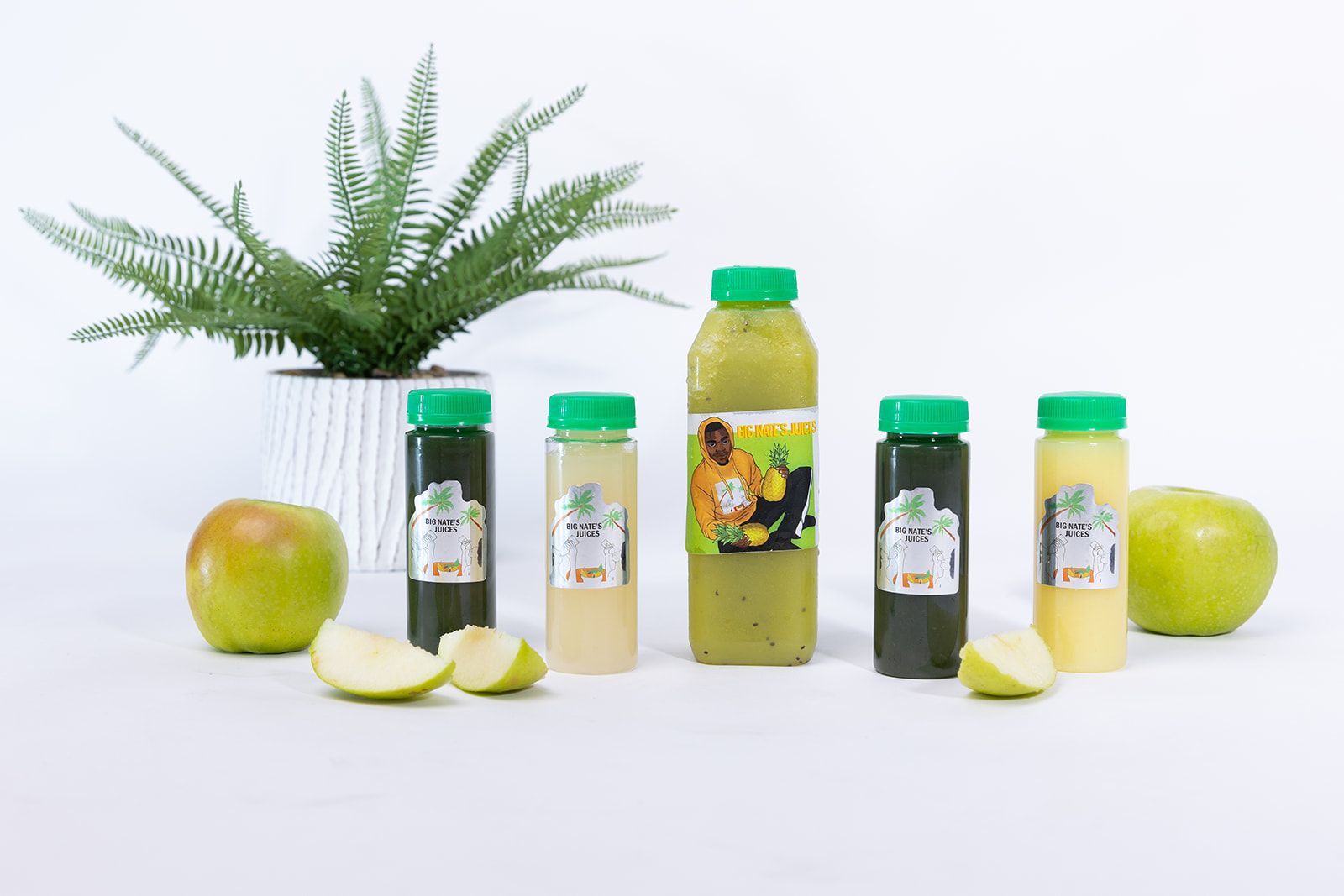 Photo of cut up green apple slices, a green plant, a kiwi smoothie, and four immunity shots from Big Nate's philly pressed juice company.