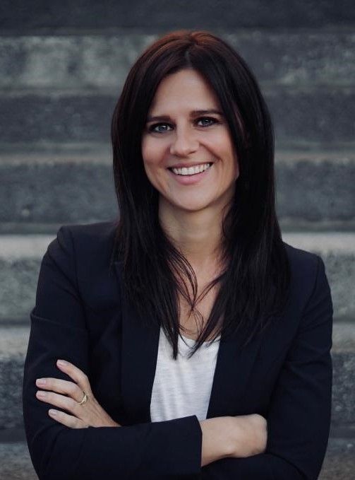 Lächelnde dunkelhaarige Frau, Referentin Marketing, schwarzer Blazer, weiße Bluse, Stufen im Hintergrund