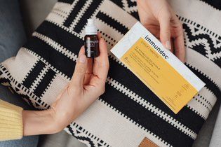 Frauenhand mit immundoc Fläschchen und Packung in der Hand