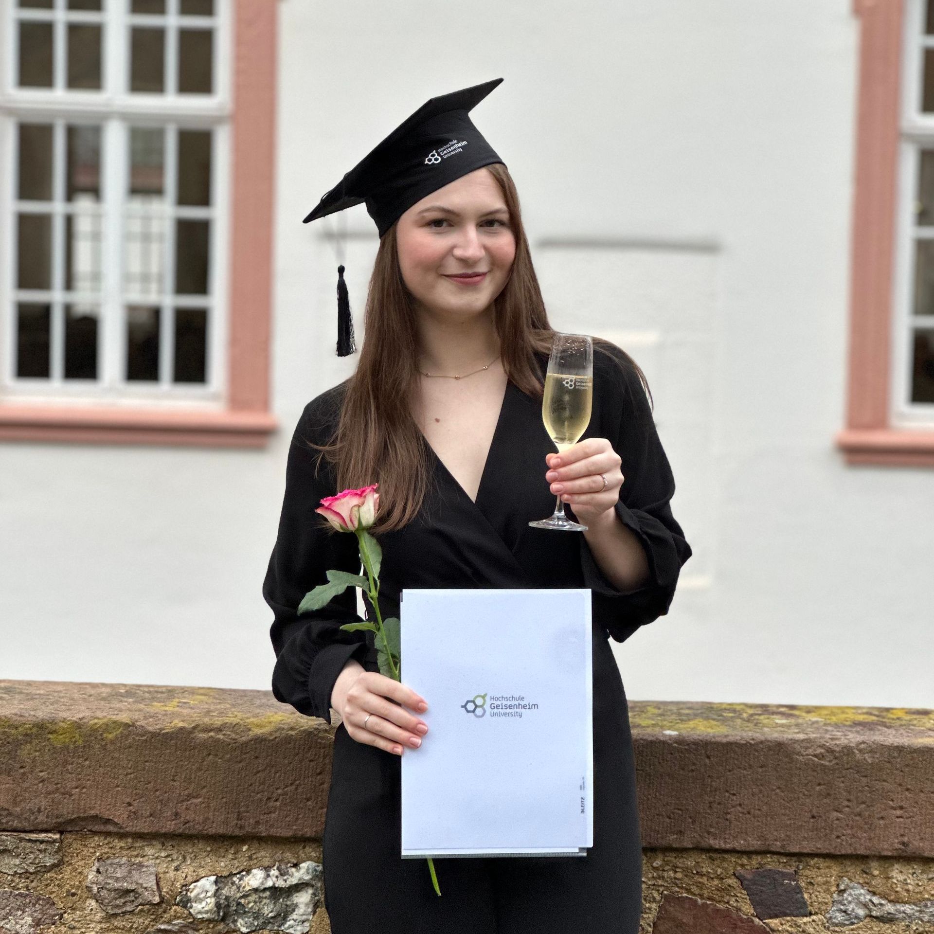 Eine junge Frau mit Bachelor-Abschluss in der Hand und Bachelor-Kappe auf dem Kopf.