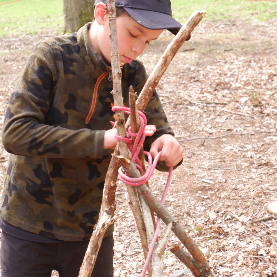 Child tying a rope around some branches to create a natural den