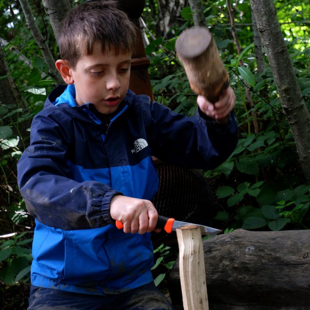 Child with mallet raised ready to strike a whittling knife into a piece of wood