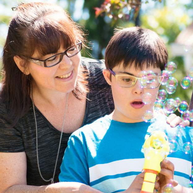 Carer and child with downs syndrome playing with bubble gun