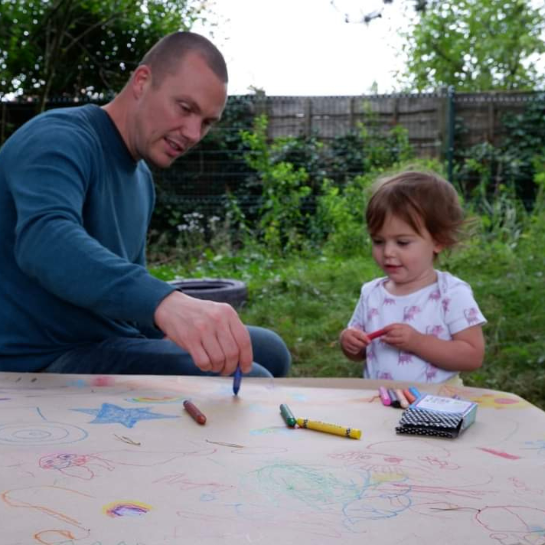 Carer and child outside drawing together with crayons