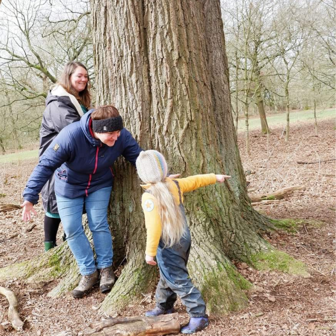 Carers and child together hiding behind a tree
