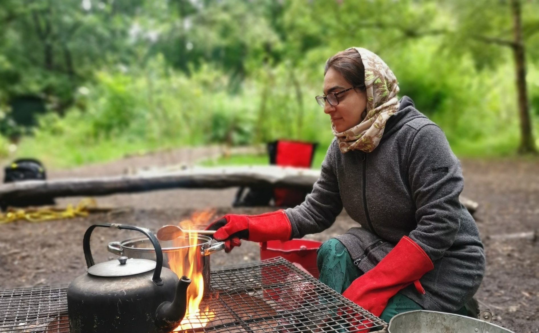 Woman with wooden spoon in hand cooking over the fire pit