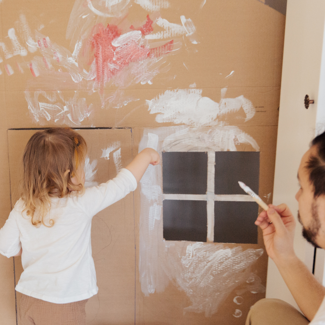 child with a carer painting a cardboard house
