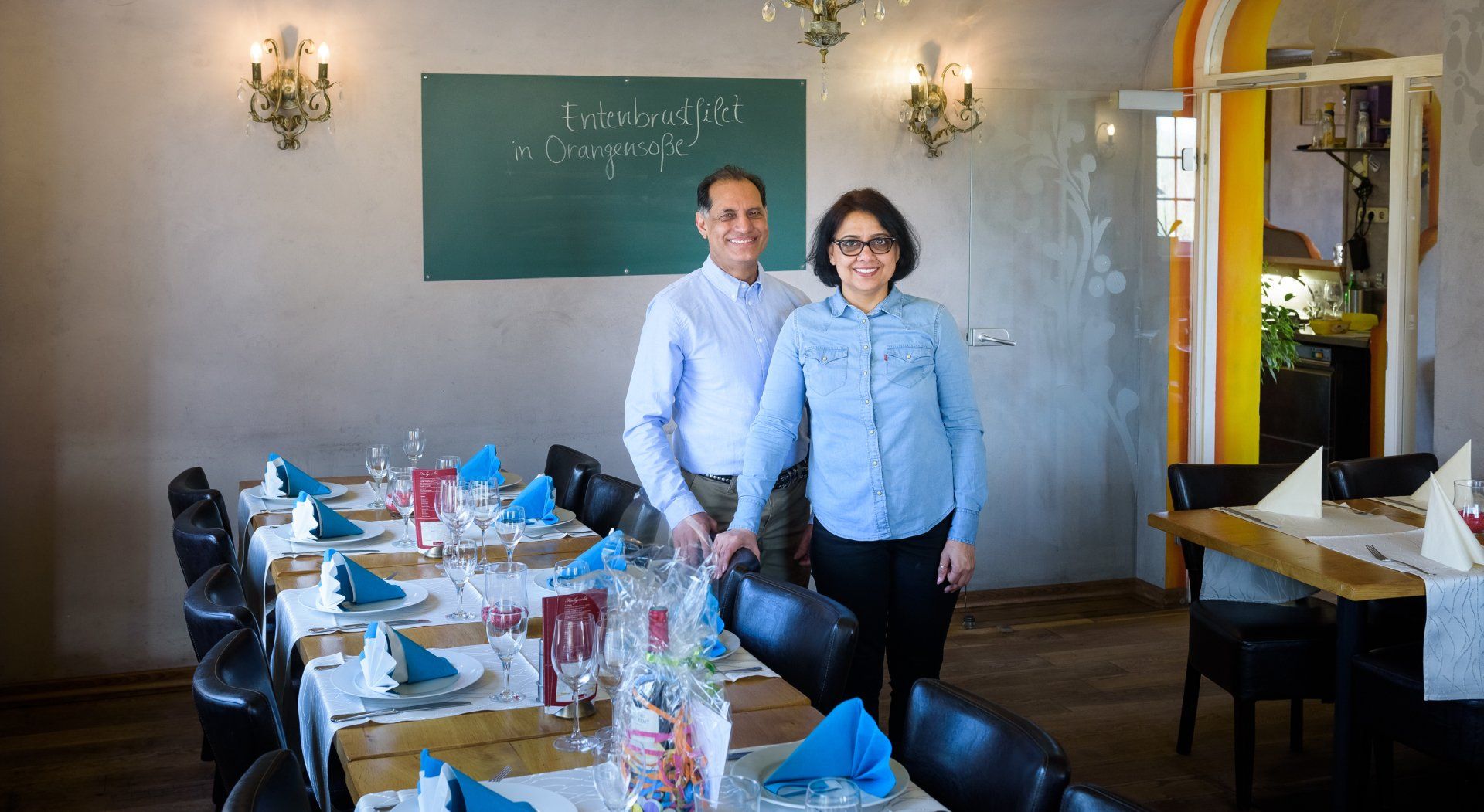 Restaurant-Inhaberin und Inhaber stehen an einer gedeckten Tafel