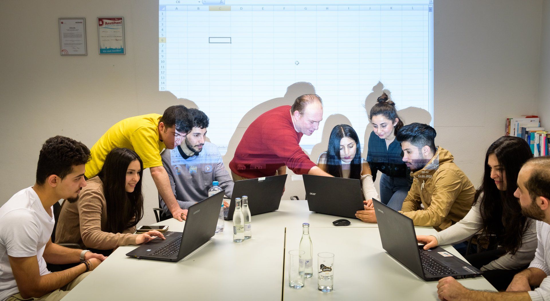 Eine Gruppe junger Leute arbeitet an einem Tisch miteinander, an dem mehrere Laptops stehen.