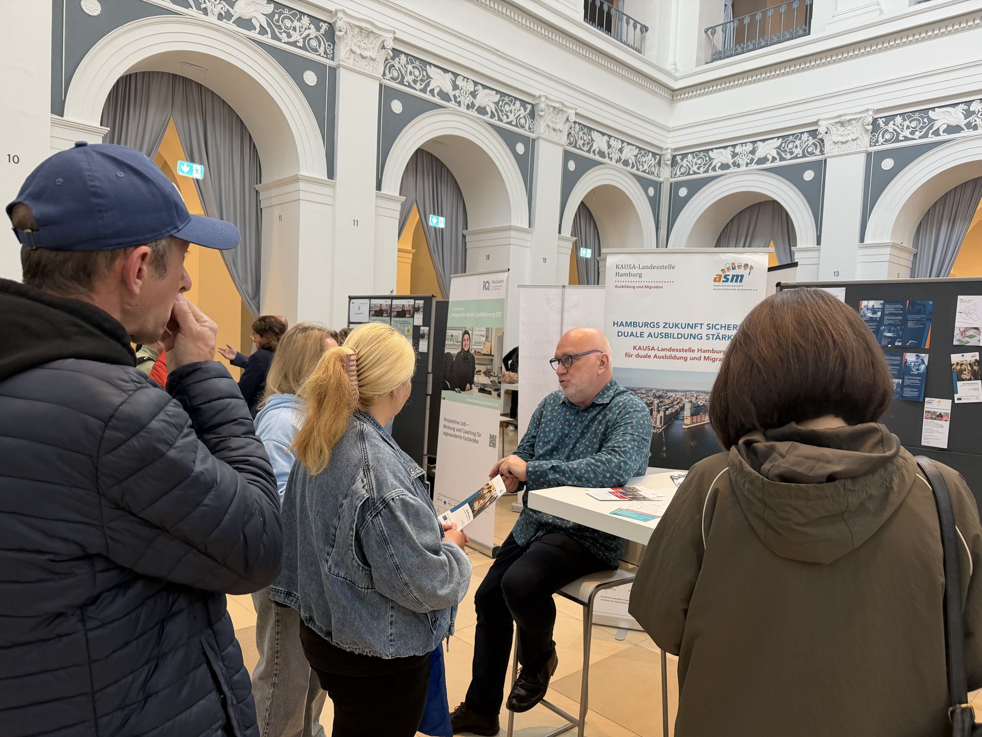 Ratsuchende stehen am Stand von ASM e. V. rund um einen Berater herum.