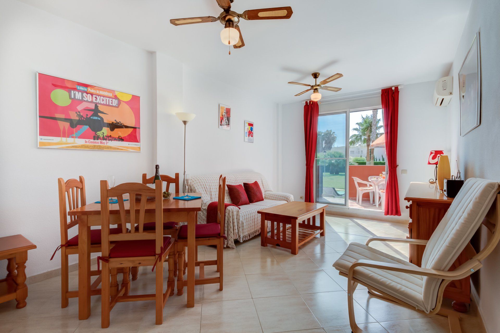 bright living dining room in white and red colour scheme with patio doors looking onto terrace and palm trees