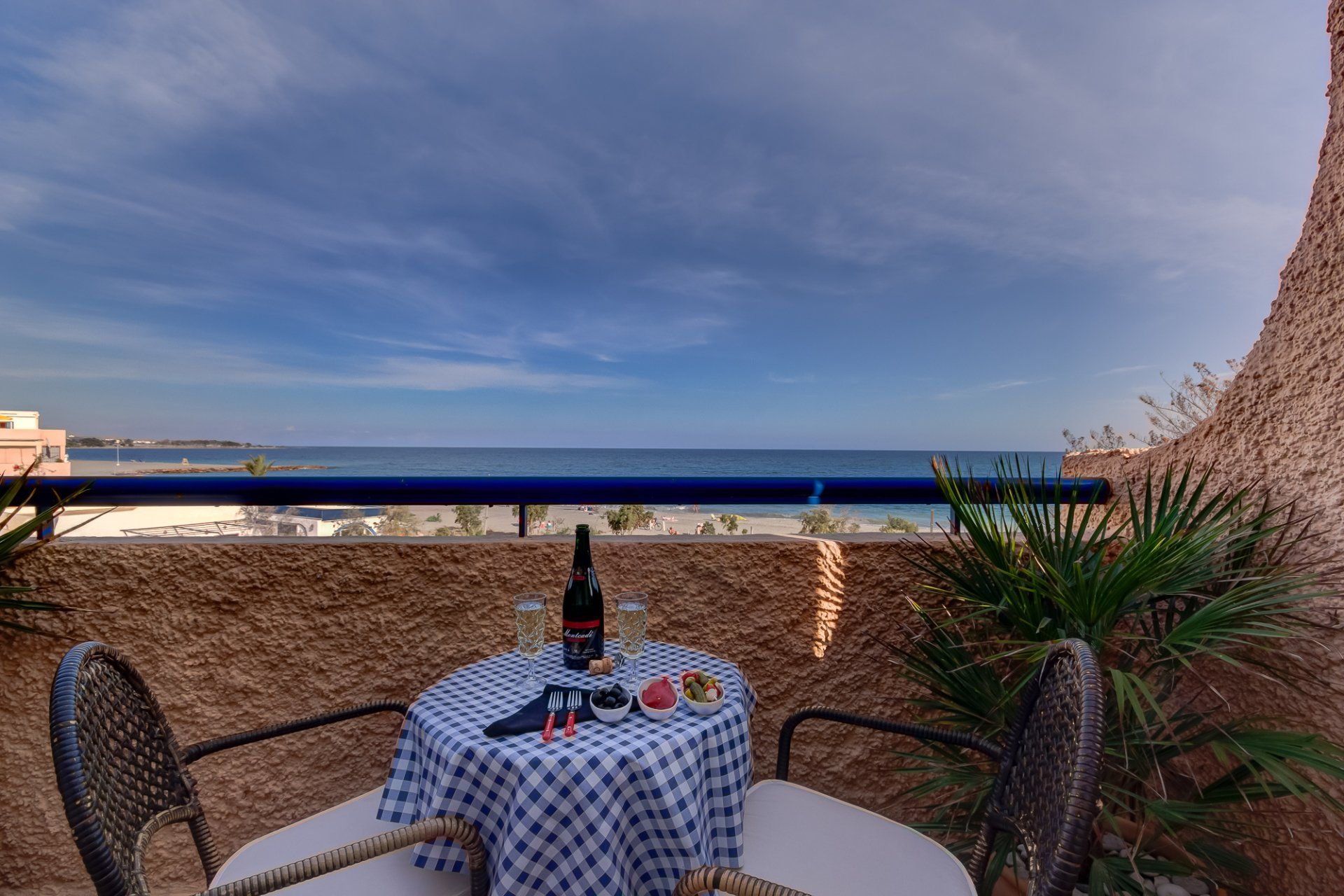 on the terrace with a bistro table and chairs and a bottle with two glasses of cava and a sea view