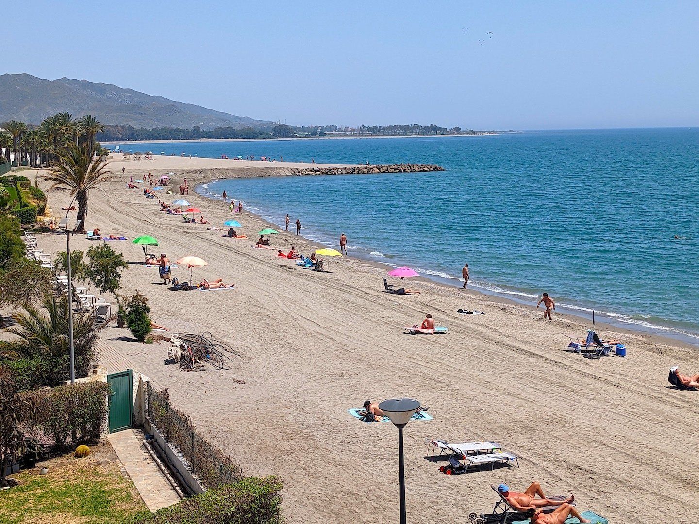 long sandy beach with palm trees, sunbathers and multi-coloured sun umbrellas