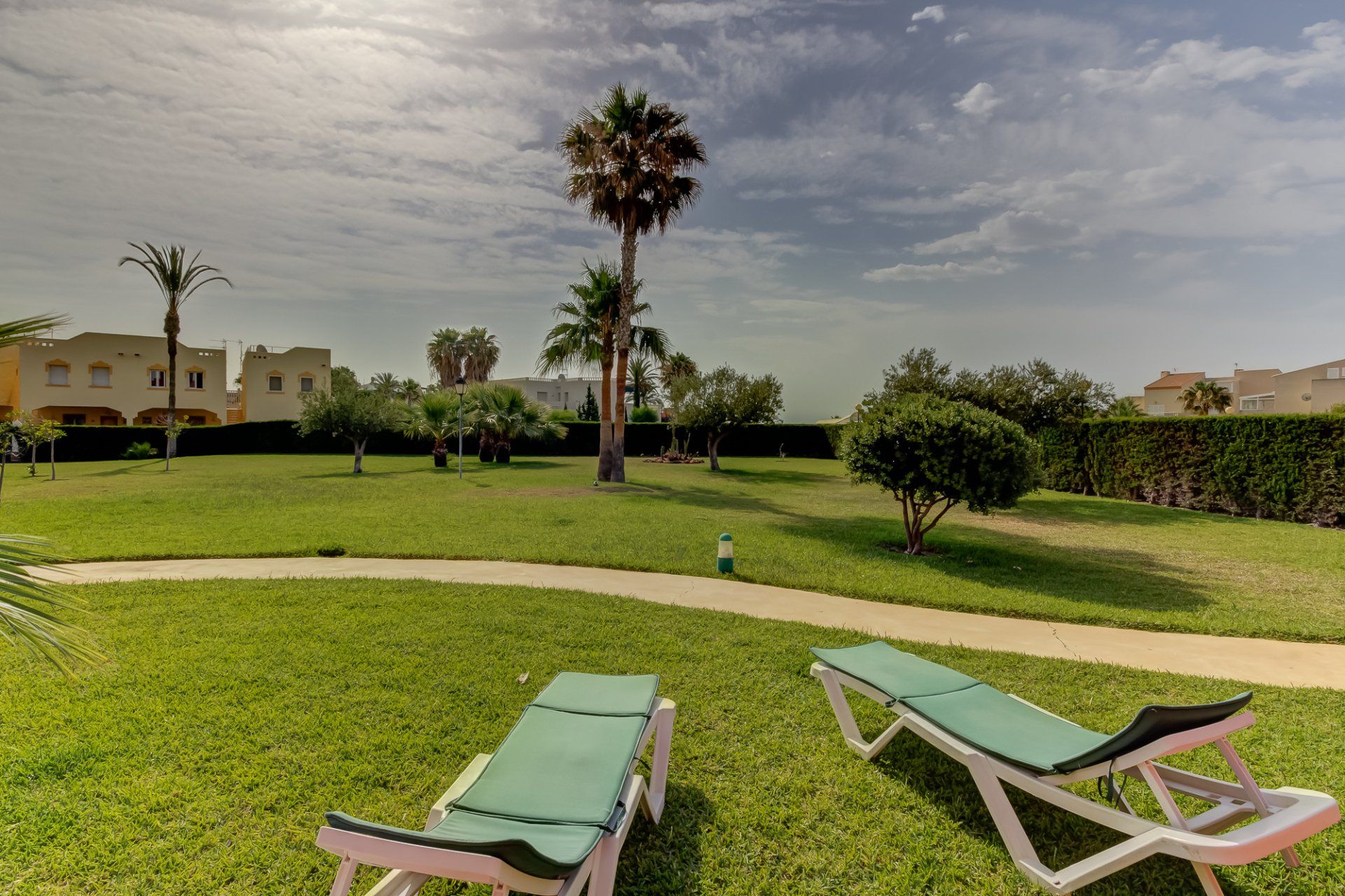 two empty sunloungers look out onto lawns with tropical plants