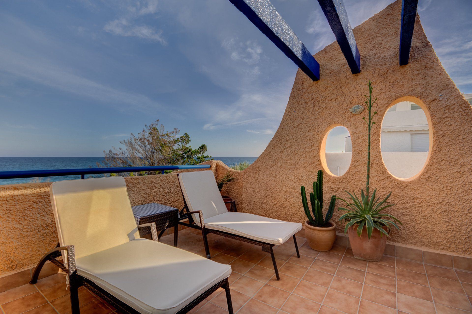 two sun loungers side by side and a drinks table in between them both and at the far end of the terrace are two big cactus plants in pots