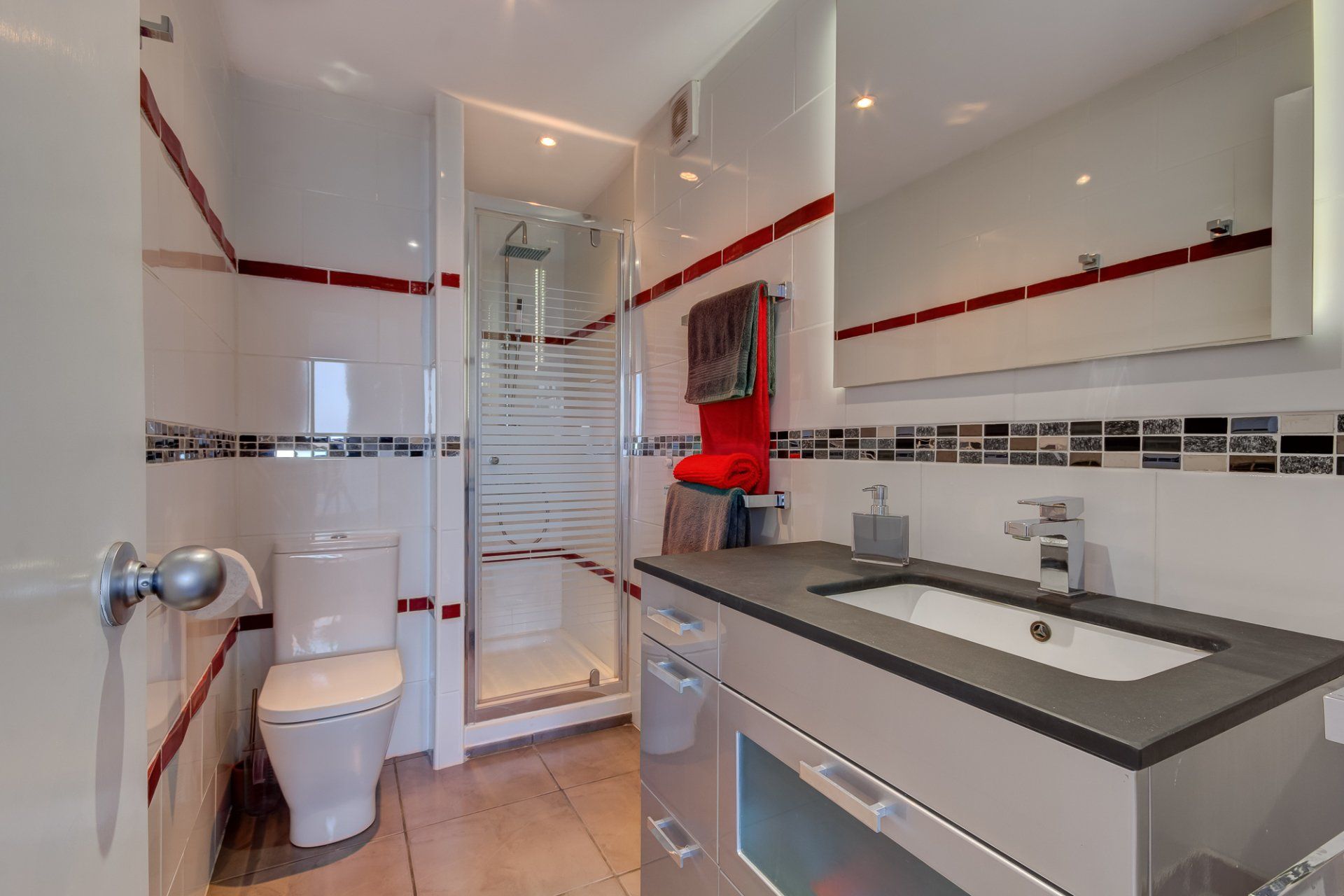 stylish and modern bathroom with white shiney tiles with red detailing and shower cubicle